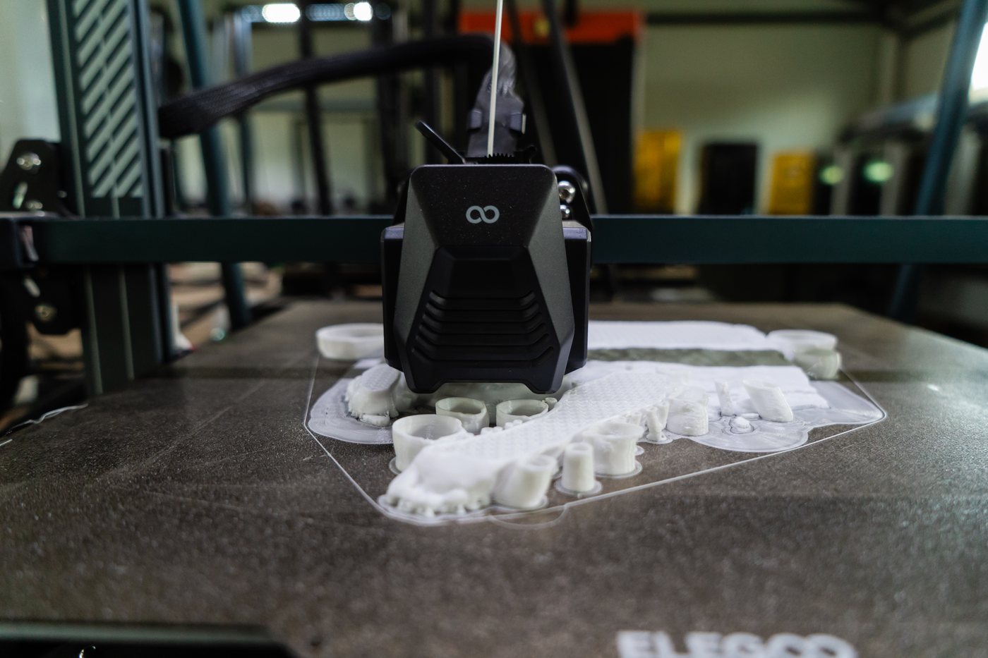 Batch of small white printed bushings, sleeves and textured panels nested together on a single build plate beneath the print head