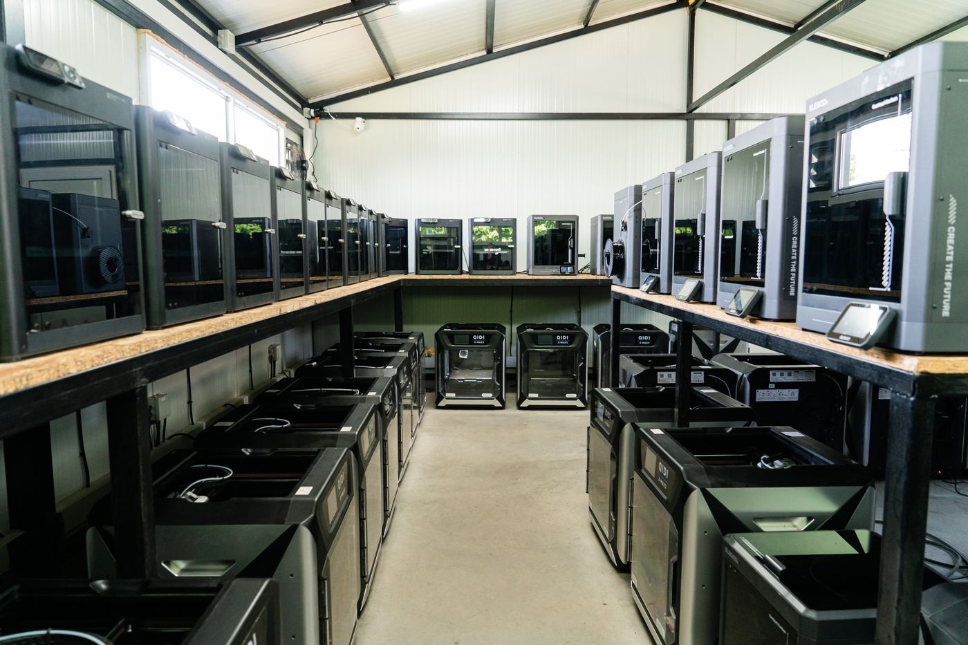 Central aisle of the production hall with a run of enclosed FDM printers down each side, on the upper shelves and at floor level